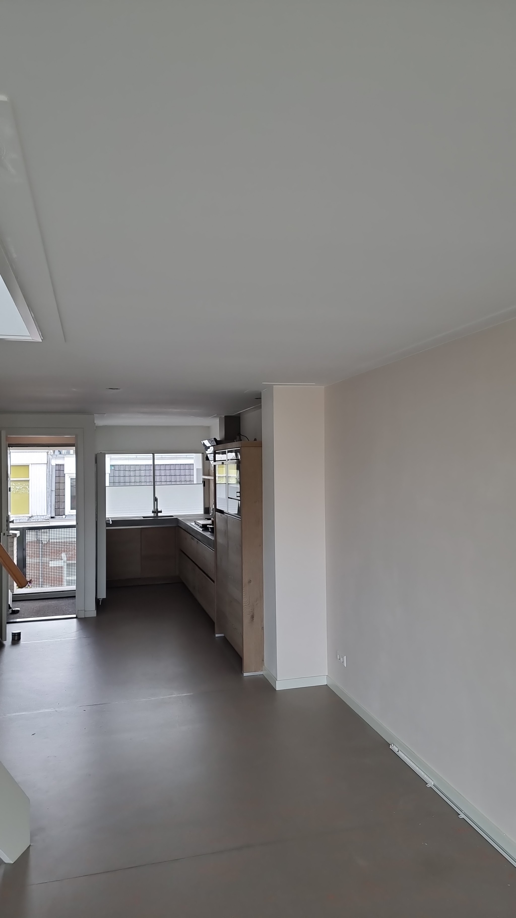 Lege open woonruimte met strak gespoten plafond en wanden, keuken op de achtergrond