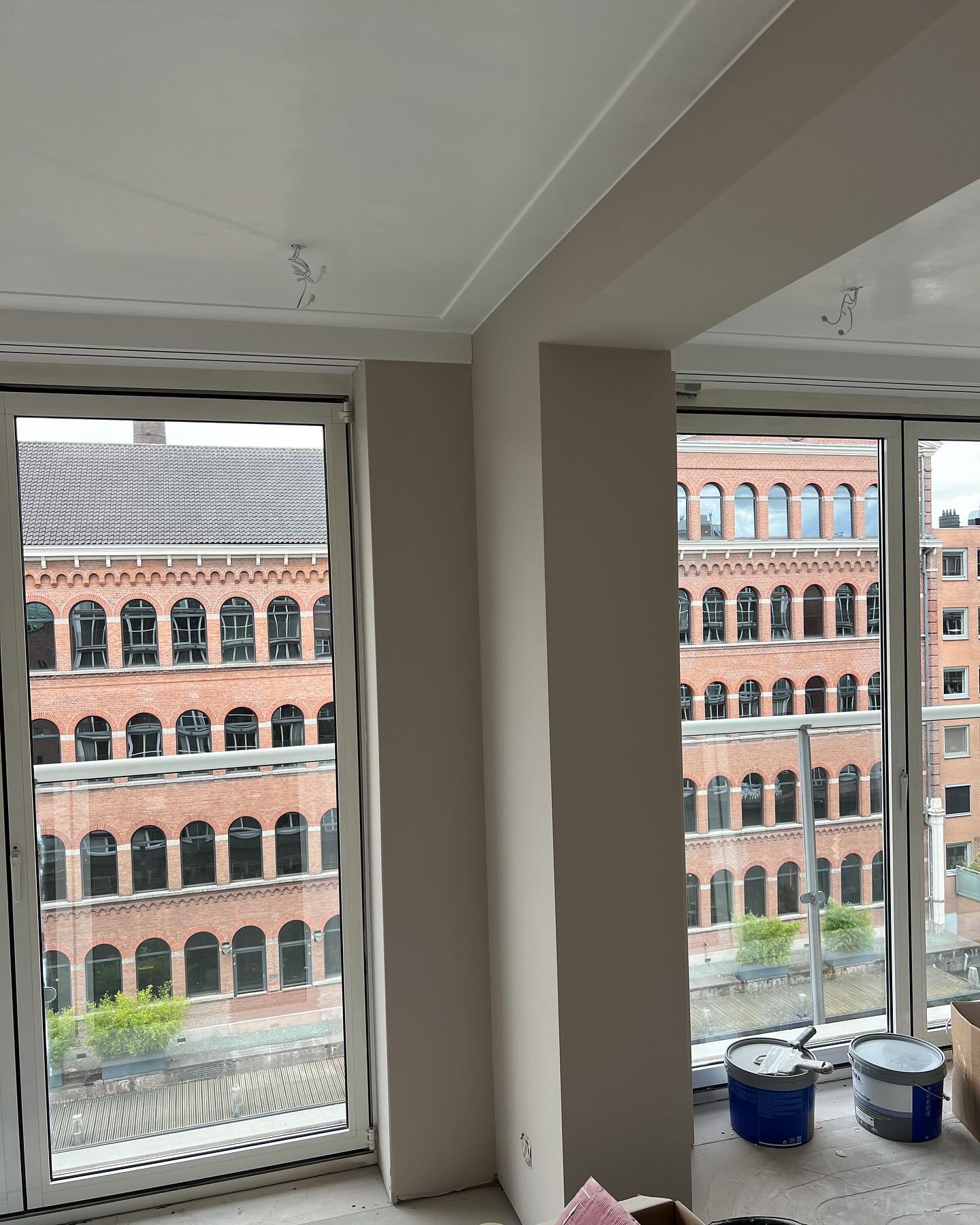 Appartement met hoge ramen, strak plafond en koof, twee verfemmers op de vensterbank